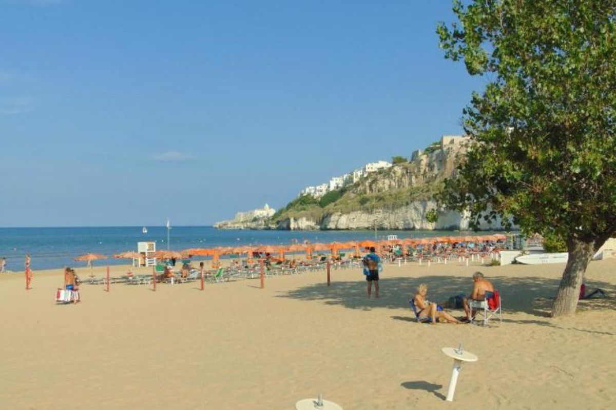 Tramonto sulla spiaggia del Pizzomunno a Vieste, con gente che passeggia e colori caldi