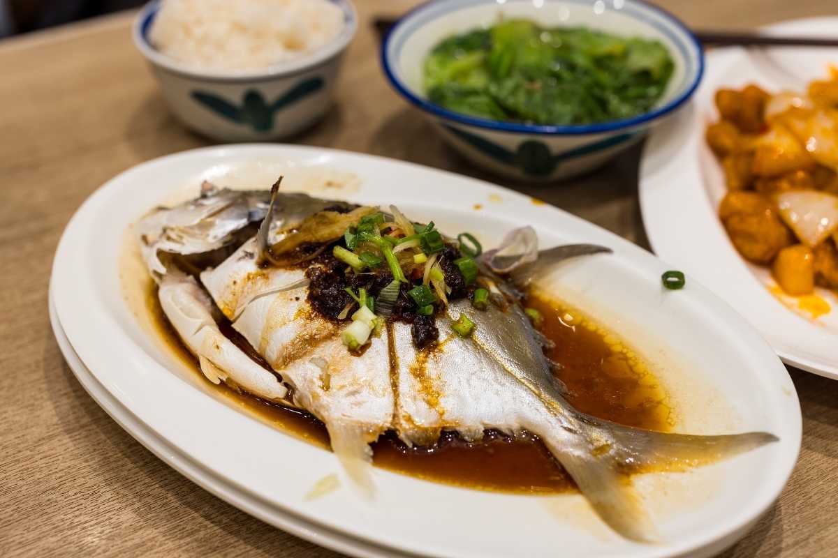 Street food di pesce a Vieste: mani che servono cartocci di frittura mista davanti a una bancarella colorata, sullo sfondo la spiaggia e il mare