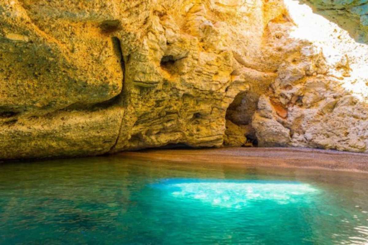 Barca in escursione davanti alle grotte marine di Vieste, acqua cristallina, falesia bianca, cielo azzurro, turisti entusiasti